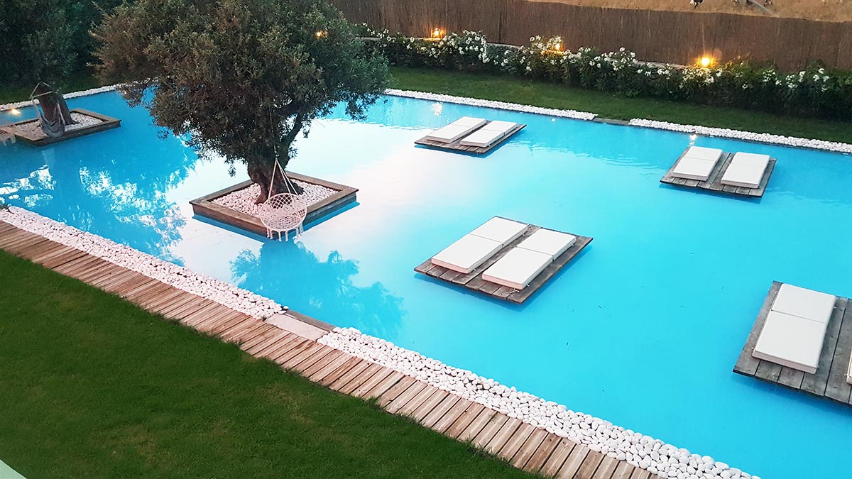 Pool lounge in evening light with floating loungers and olive tree